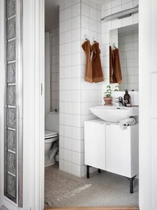 A minimalist bathroom with white tiles, a sink, and a toilet.