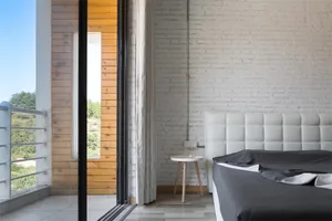 A minimalist bedroom featuring a white brick wall, wooden flooring, and a bed with a grey cover.