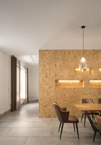 A minimalist dining room with a wooden table and brown leather chairs, featuring a unique wall composed of oriented strand bo