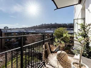 Modern balcony with steel railing, wooden furniture, and potted plants.