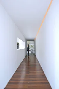 簡約走廊，木地板與白牆，遠處站著一位男子。