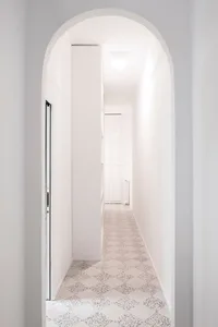 A minimalistic white hallway with patterned white and black tiles on the floor and white walls.