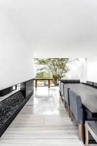 A modern minimalist dining room featuring concrete flooring and walls, with a long dining table, grey upholstered chairs, and