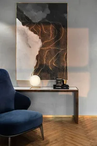 A modern interior design with metallic artwork, wood flooring, a blue armchair, and a brass table lamp.