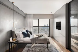 Modern minimalist bedroom with a large bed, white and gray pillows, and a view of the city through the window.