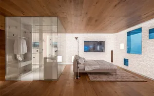 A minimalist bedroom featuring wooden furniture and a glass-enclosed shower area.