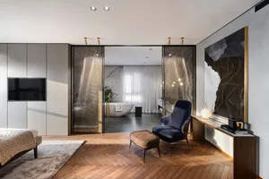 Modern bedroom suite featuring a glass door and a blue velvet armchair.