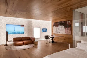 A modern bedroom with wooden flooring, a brown leather sofa, a round table, and a painting on the wall.