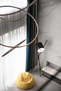 A modern living room featuring a yellow pouf seating, a black tripod floor lamp, and a marble wall with textured accents.