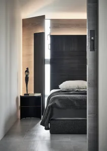 Modern minimalist bedroom with dark wood walls, a black bed frame, and a single sculpture on the nightstand.