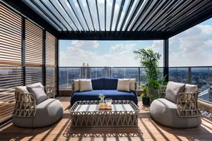 現代屋頂露台，擺放藍色沙發、兩張扶手椅、咖啡桌及盆栽，透過大型窗戶可欣賞城市景觀