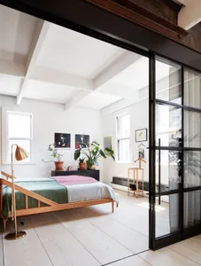 Modern minimalist bedroom with wooden furniture, plants, and a large window.