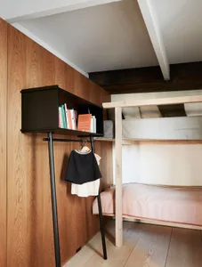 A minimalist bedroom with wooden walls and furniture, featuring a bunk bed and a black freestanding wardrobe.