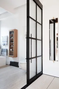 A modern bathroom with white furniture and a frosted glass door.