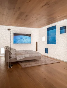 A modern bedroom featuring a wooden floor, a bed with a white blanket and pillows, and framed blue artworks on the wall.