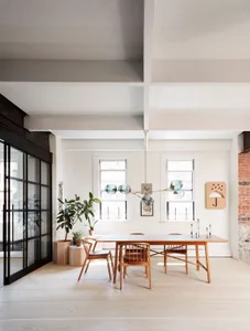A modern dining room with a wooden table, brick wall, and a mid-century modern light fixture hanging above it.