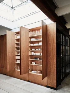A modern kitchen with a wooden storage unit displaying dishes, glasses, and other kitchenware.