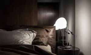 A dark bedroom with pillows on a bed and a bright light shining onto a wall.
