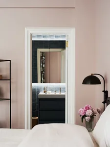 A minimalist bedroom with a pink wall, white furniture, and a mirror.
