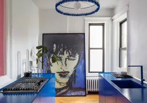 Modern kitchen with blue countertops, white appliances, and a large abstract painting of a face.