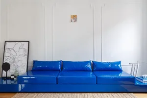 A minimalist living space featuring a bright blue PVC sofa and abstract artwork on the wall.