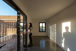 A minimalist room with concrete walls, floor, and ceiling, featuring a window with a shadow pattern on the wall.
