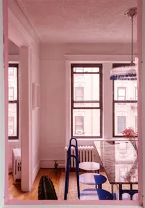 Minimalist living room with pink walls, metallic finishes, and a large window overlooking a cityscape.