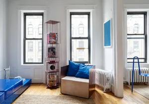 A minimalist living room with a metal bookshelf, wooden floor, and upholstered seating.
