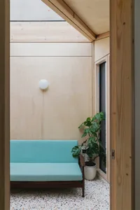 A minimalist living space featuring wooden walls, turquoise fabric seating, and a concrete floor with a potted plant.
