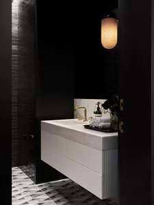 A modern bathroom featuring a white countertop with a brass faucet and a patterned marble floor.