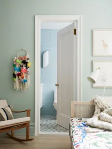 A bedroom with a wooden bed, colorful fabric, and yarn decoration against a pastel green wall.