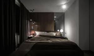 A modern bedroom featuring a wooden panel wall, a queen-sized bed with a dark comforter, and two bedside lamps.