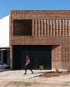 A woman walking in front of a modern brick building with a black garage door and large window.
