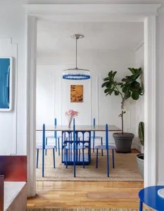 Modern dining room with a blue table and chairs, glass chandelier, and indoor plants.