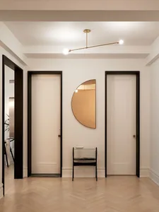 A modern entrance hall featuring hardwood floors, white doors with black frames, a half-circle mirror, and a small glass tabl