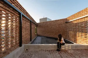 Person sitting on a modern exterior brick wall with a rooftop pool and surrounding cityscape in the background.