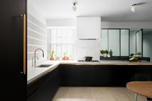 A modern kitchen with marble countertops and glass cabinets, featuring black cabinetry and a wooden dining table.