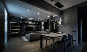 A modern living room with a concrete wall and a dark, minimalist interior design featuring a gray sofa and a dining table.