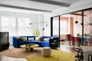 Modern living room with a blue sofa, multiple pillows, a round wooden coffee table, and a yellow carpet