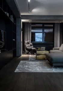 A modern living room with dark wooden floors, a cozy grey sofa, and a stylish armchair, featuring a large bookshelf, a wooden