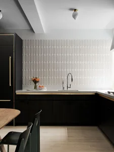 Modern minimalist kitchen with a white ceramic tile backsplash, featuring black cabinetry, a white countertop, and a sleek fa