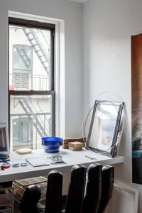 A minimalist home office with white walls, a white desk, and black office chairs.