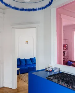 Bright minimalistic living room with blue walls, couch, and cushions, accented by a pink wall and white-framed doorway.