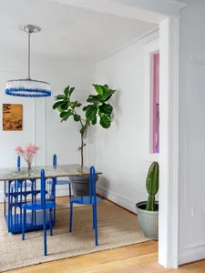 A minimalist dining room with a metallic dining table, blue chairs, and potted plants.