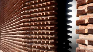 A wall composed of neatly arranged red bricks under natural light, casting a shadow of bricks on a white surface.