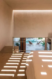 A modern bedroom featuring textured concrete walls and natural light streaming through the ceiling.
