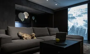A cozy modern industrial living room with dark walls, a large dark sectional sofa, a coffee table with an apple, and a projec