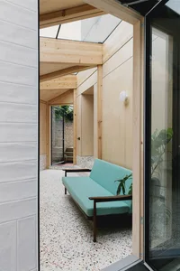 Modern interior design featuring a teal sofa, wooden beams, glass ceiling, and terrazzo floor.