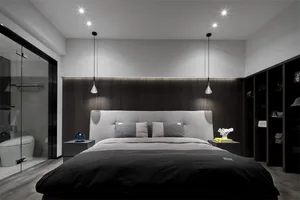 Minimalist bedroom with a large bed, gray headboard, and black and gray bedding. Modern lighting fixtures and a bathroom area