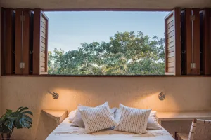 A cozy, modern bedroom with a large window overlooking lush greenery, illuminated by warm sconces.